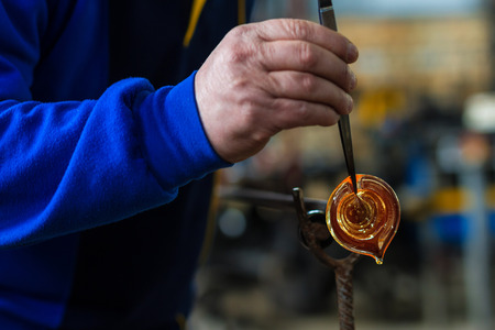 Glass blower forming beautiful piece of glass. A glass crafter is burning and blowing an art piece.
