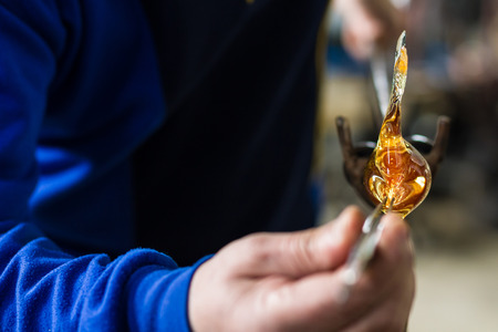 Glass blower forming beautiful piece of glass. A glass crafter is burning and blowing an art piece.の写真素材