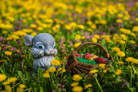 Easter eggs in basket with rabbit on green grass meadow with flowers