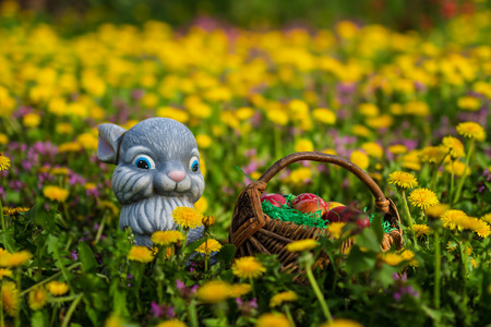 Easter eggs in basket with rabbit on green grass meadow with flowersの写真素材