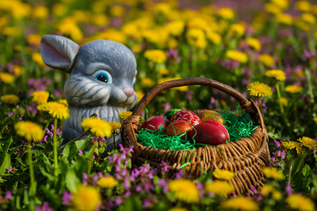 Easter eggs in basket with rabbit on green grass meadow with flowersの写真素材