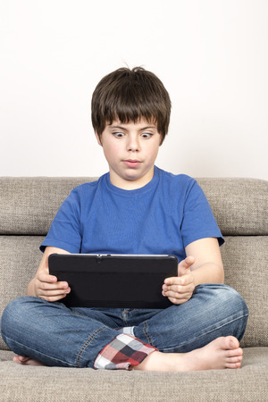 Surprised Young boy with eyes wide open using tablet digital on the sofa の写真素材