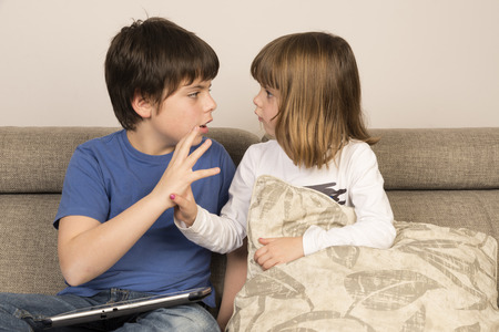 Kids arguing for playing with a digital tablet on a sofa の写真素材