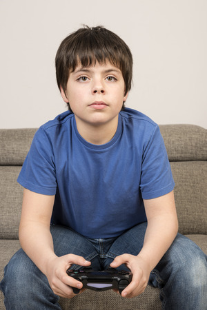 Young boy 10 years playing videogame sitting on sofa with watchful eyesの写真素材