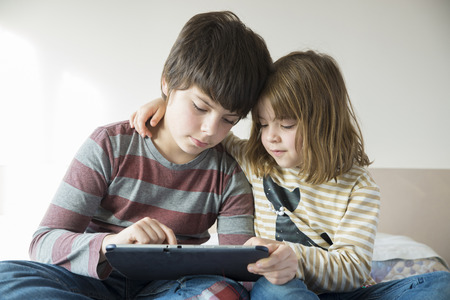 Children playing with a digital tablet on the bedの写真素材