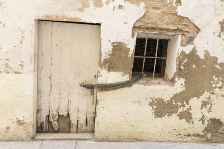 old house wall with white door and window together with a chain and padlockの写真素材