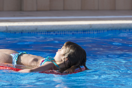 Little girl on an inflatable mattress in a swimming poolの写真素材