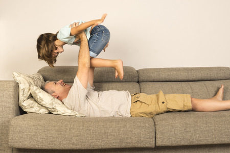 man lying on sofa and lifting up his daughterの写真素材