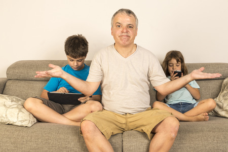children sitting on the sofa playing while his father does not know what to do 