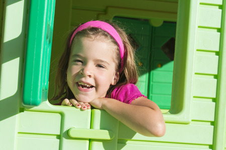 Little girl smiling in plastic house window at playground の写真素材