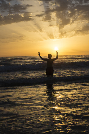 boy bathing on the beach at dusk on a beach in Andalusia, Spain. The child is doing the victory signの写真素材