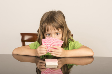 portrait of smiling little girl playing cards with squintの写真素材