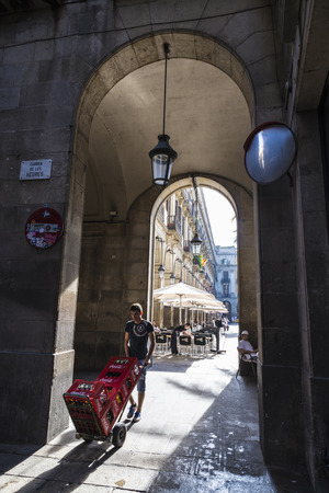 Barcelona, Spain - October 17, 2014: A deliveryman pushing a shopping boxes of coke as a waiter clean a table and a chef lies in Placa Reialのeditorial素材