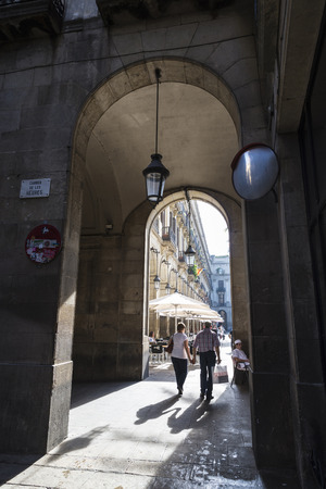 Barcelona, Spain - October 17, 2014: A mature couple walking holding hands while a cook rests under the arcades of Placa Reialのeditorial素材
