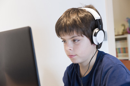 Child looking at a laptop screen carefully and listening through headphones audioの写真素材