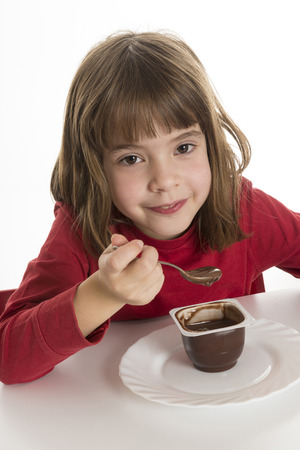Little girl eating a chocolate custard isolated on white backgroundの写真素材