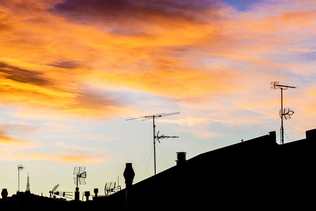 Silhouettes of antennas backlit at sunset with colorful sky cloudsの写真素材
