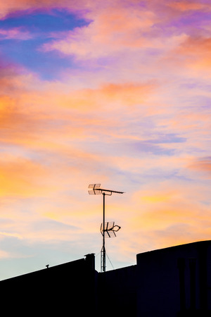 Silhouettes of antennas backlit at sunset with colorful sky cloudsの写真素材