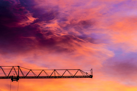 Silhouette of a construction crane at sunset with colorful sky cloudsの写真素材