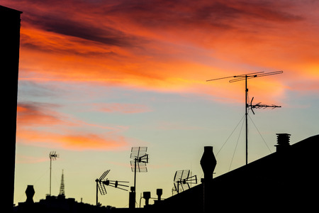 Silhouettes of antennas and chimneys backlit at sunset with colorful sky cloudsの写真素材