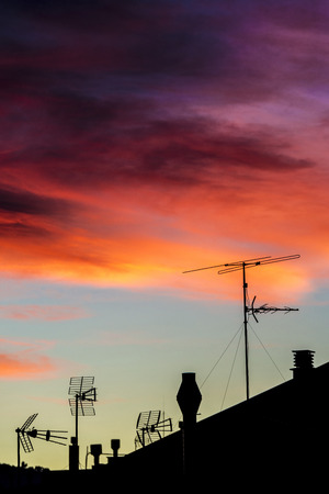 Silhouettes of antennas and chimneys backlit at sunset with colorful sky cloudsの写真素材