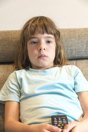 Little girl with TV remote control watching TV sitting on the couchの写真素材