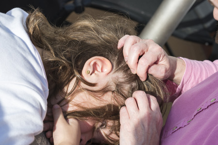 Mother looking for head lice at her little daughter to sunlight