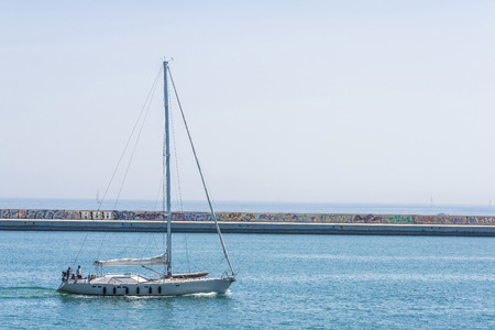 Barcelona, Spain - May 2, 2015: Sailboat sailing out of the harbor and the breakwater full of graffiti in the backgroundのeditorial素材