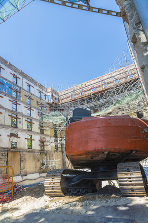 Construction of a building keeping the old facade through a system of beams in Barcelona, Catalonia, Spain. The workers and their bulldozers are doing the foundations of the new buildingの写真素材