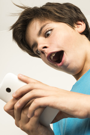Boy touching a mobile phone with a look of surprise isolated on white backgroundの写真素材