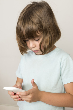 Little girl touching a mobile phone isolated on white backgroundの写真素材