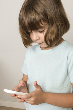 Little girl touching a mobile phone isolated on white backgroundの写真素材