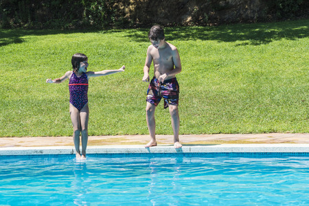 Little girl jumping in pump in an outdoor pool while her brother jumps not making a jokeの写真素材