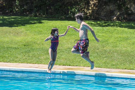 Children jumping together in an outdoor pool holding handsの写真素材