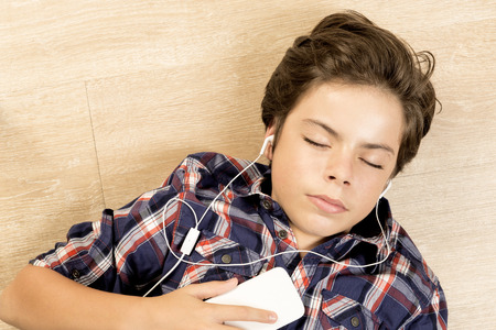 Portrait of a boy listening to music with headphones stretched on a parquet floor at homeの写真素材