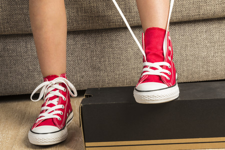 Little girl tying a pair of red sneakers at homeの写真素材
