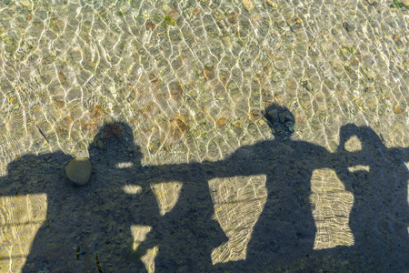 Shadows of the members of a family reflected in a river while watching from a bridgeの写真素材
