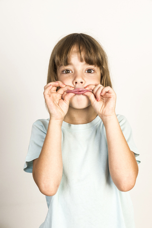 Happy little girl grimacing with fingers clenched lips at home isolated on white backgroundの写真素材