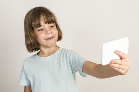 Happy little girl take a selfie with a smartphone at home isolated on white backgroundの写真素材
