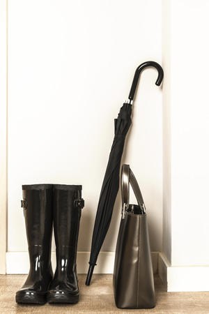 Black wellies, umbrella and bag ready for use in a rainy dayの写真素材