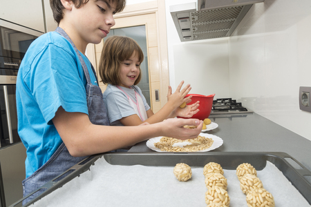 Little girl and young boy kneading marzipan for make panellets  in the kitchen. Panellet are traditional desserts of All Saints holiday, known as Castanyada in Catalonia, Spainの写真素材