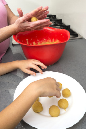Mother and daughter kneading marzipan for make panellets  in the kitchen. Panellet are traditional desserts of All Saints holiday, known as Castanyada in Catalonia, Spainの写真素材