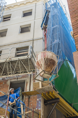 Barcelona, Spain - June 4, 2015: Worker running a construction crane is lifting a container of cement in the construction of a building in the old town of Barcelonaのeditorial素材