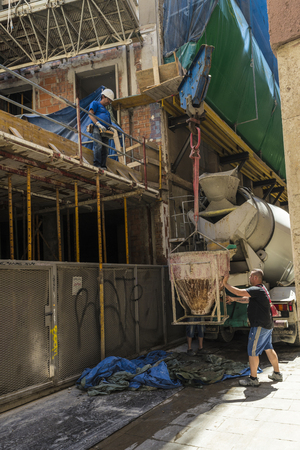 Barcelona, Spain - June 4, 2015: Workers running a construction crane is lifting a container of cement in the construction of a building in the old town of Barcelonaのeditorial素材