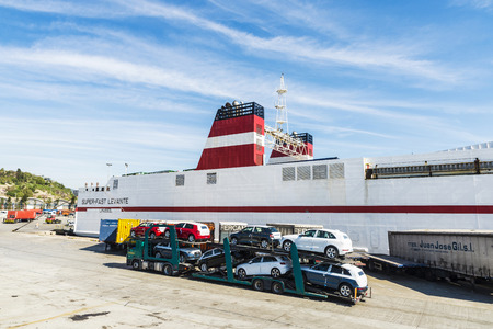 Barcelona, Spain - April 19, 2016: White cargo ship moored in the port of Barcelona with containers parked ready for shipping while passing a truck loaded with new cars in Barcelona, Catalonia, Spainのeditorial素材