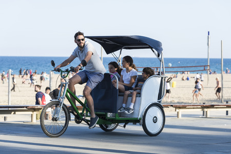 Barcelona, Spain - June 1, 2016: Barcelona promenade full of people walking or playing sports. it stands a parent taking their children on a tricycle rickshawのeditorial素材