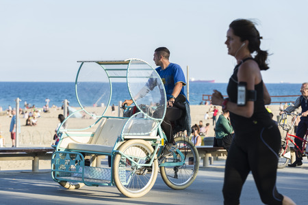 Barcelona, Spain - June 1, 2016: Barcelona promenade full of people walking or playing sports. In the foreground a young man in a rickshaw tricycleのeditorial素材