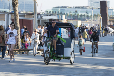 Barcelona, Spain - June 1, 2016: Barcelona promenade full of people walking or playing sports. In the foreground a young man in a rickshaw tricycleのeditorial素材