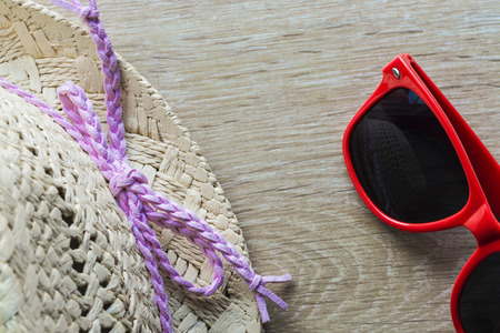 Straw hat with a pink bow and a red sunglasses on wooden floorの写真素材
