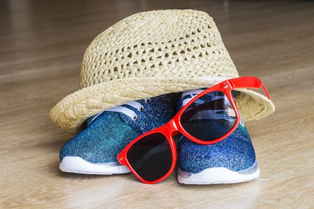 Blue bright sneakers and straw hat with red sunglasses for girl on wooden floorの写真素材